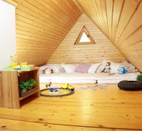 The attic space of the cottage with a wooden decor floor contains mattresses, toys, and a table.