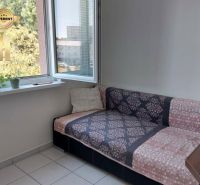 A sofa in the corner of the room with an open window and flowers on the windowsill.