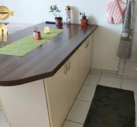 A kitchen unit with an island in a studio apartment, white tiles and decorations.