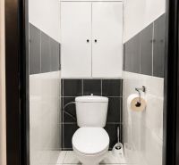 A bathroom with white and gray tiles, storage space above the toilet.