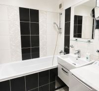 Bathroom with a bathtub, sink, and washing machine in a 2-room apartment. Black and white tiles.