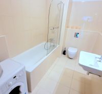 A bathroom with a bathtub and a washing machine in a 2-room apartment, light tiles, sink.