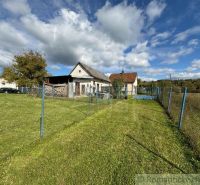 A family house in Volica surrounded by a green lawn and a blue fence under a blue sky.