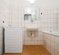 Bathroom in a 2-room apartment with a washing machine, sink, bathtub, and white tiles.