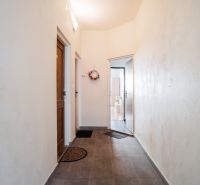 A hallway in a 2-room apartment with tiles, an entrance door, and a decorative wreath on the wall.