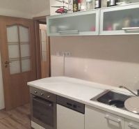 A kitchen in a 2-room apartment with a sink, stove, and storage cabinets.