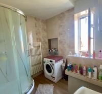 The bathroom with a washing machine and a shower in the studio apartment has a floor with a wooden decor.
