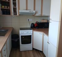 A kitchen in a studio apartment with a wooden decor floor and white cabinets.