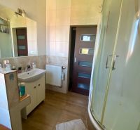 Bathroom with a corner shower, light ceramic tiles, and a sink in a studio apartment.