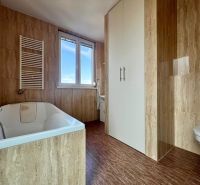 A bathroom with a bathtub and a wooden decor floor in a 2-room apartment.
