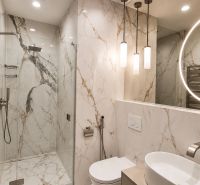 A bathroom with marble tiles in a 2-room apartment, featuring a large mirror and a shower corner.