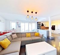 Living room with an open kitchen, wooden decor flooring, and comfortable seating in a three-room apartment.