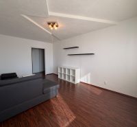 Living room in a three-room apartment with a wooden decor floor, gray sofa, and shelves.