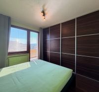 A bedroom in a three-room apartment with a wood-patterned floor and a large built-in wardrobe.