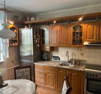 A kitchen in a 3-room apartment with wooden furniture, a decorative curtain, and a dining table.