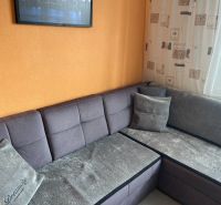 Gray sofa in the corner of the living room in a three-room apartment with an orange wall.