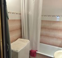 Bathroom with a bathtub, washing machine with a towel, and tiles in a 3-room apartment.