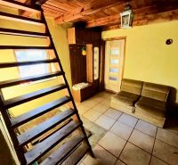 The interior of a cabin with wooden stairs, a couch, and tiled flooring.