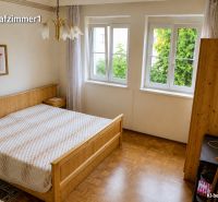 Bedroom in a family house with wood-patterned flooring, a large window, and a bed.