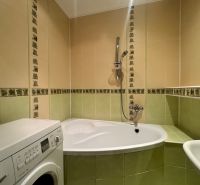 Bathroom in a 4-room apartment with a bathtub and a washing machine, green-cream tiles.