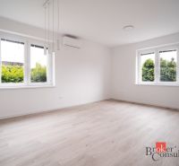 A bright room with wood-patterned flooring and large windows in a three-room apartment.