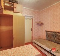 A room in a family house with a bed, a wardrobe, and pink wallpaper.