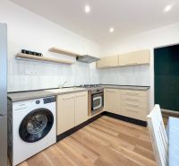 A kitchen in a 2-room apartment with a wooden decor floor, light furniture, and appliances.