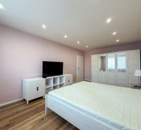 A bedroom in a two-room apartment with a wooden decor floor and white furniture.