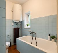 A bathroom in a family house with a bathtub, blue tiles, and a water heater on the wall.