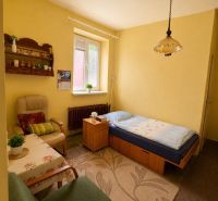 A room in a family house: bed, chairs, table, carpet, and window with blinds.