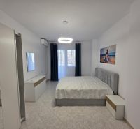 Bedroom in a 2-room apartment with a bed, white furniture, and a painting on the wall.