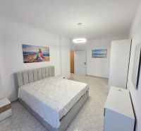 A bright bedroom in a two-room apartment with artistic paintings and white furniture.