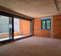 An unfinished 3-room apartment with large windows and exposed bricks without flooring.