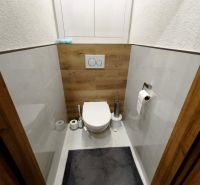 A toilet with a wooden floor decor and white tiles in a 3-room apartment.