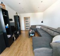 Living room with a large sofa, wooden decor flooring, and black furniture in a three-room apartment.