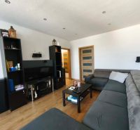 Living room in a 3-room apartment with a large sofa, television, and wooden decor flooring.