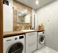Bathroom in a 3-room apartment with a washing machine, dryer, and floor with wooden decor.