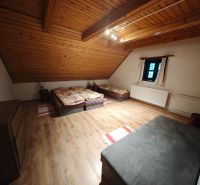 A room with three beds, a wooden decor floor, and a slanted wooden ceiling in a cottage.