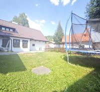 A cottage in Špania Dolina with a trampoline on a grassy garden under a blue sky.