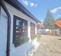 A cottage in Špania Dolina with a flower bed by the window and a paved walkway.