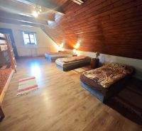 An attic room in a cottage with a wooden decor floor and multiple beds.