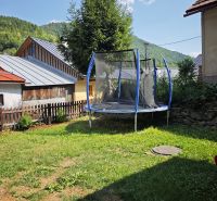 A trampoline near a cottage in Špania Dolina, surrounded by grass and trees in the background.