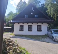 A cottage in Špania Dolina with a white facade and a satellite dish, surrounded by greenery.