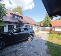 A car parked near a cottage in Špania Dolina, with visible roofs and a fence.