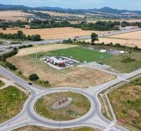 Roundabout and highway in Nová Polhora surrounded by fields and a sports field.