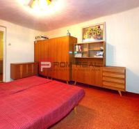 A bedroom in a family house with a red carpet, wooden furniture, and floral curtains.