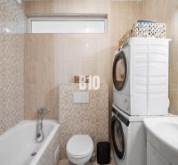 Bathroom in a 2-room apartment with a washing machine, dryer, bathtub, and toilet.