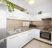 A kitchen in a 2-room apartment with white cabinets and wood decor.