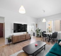 A bright living room of a two-room apartment with a wooden decor floor and a dining table.