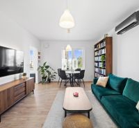 Living room in a two-room apartment with a large television, a bookshelf, and a wooden decor floor.